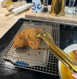 "Baloo stainless steel strainer spoon tongs lifting golden fried chicken from hot oil in a kitchen pan."