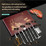 Eight-piece crab eating tool set arranged on a dark background with a wooden presentation box. The set includes metal tools such as a crab hammer, crab claw, crab hook, crab spatula, crab tweezers, and crab needle, along with gold-toned scissors and a small scraper.