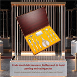 An open wooden presentation box displaying a set of stainless steel crab peeling tools and utensils on a yellow insert, shown floating above a display stand with decorative text.